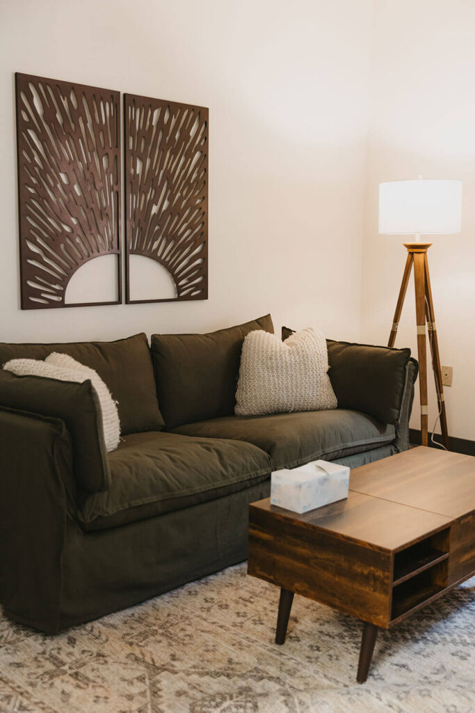 The olive sofa beneath the sunrise wood carving, tissues within reach